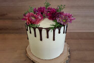 Hohe Torte mit Blumen, an deren Rändern braune Soße herunterläuft