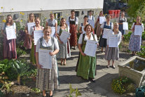 Mehrere Frauen in Dirndeln stehen mit Abstand nebeneinander und halten Zeugnis