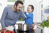 Kind hält Mann in Küche hölzernen Kochlöffel in den Mund 